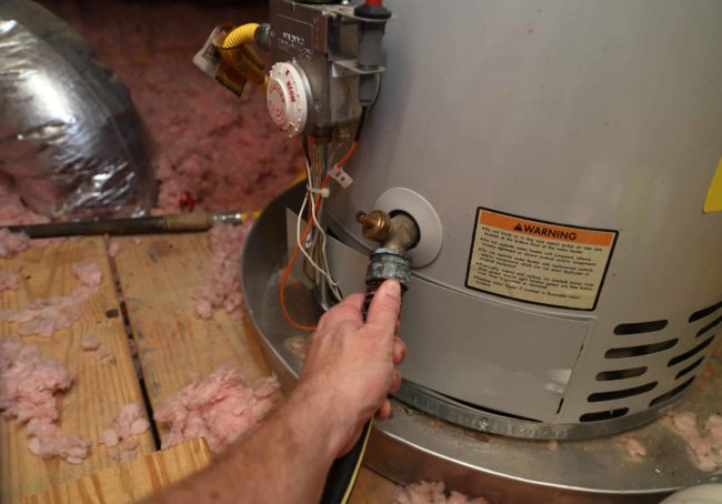 Hand attaches hose to drain water heater